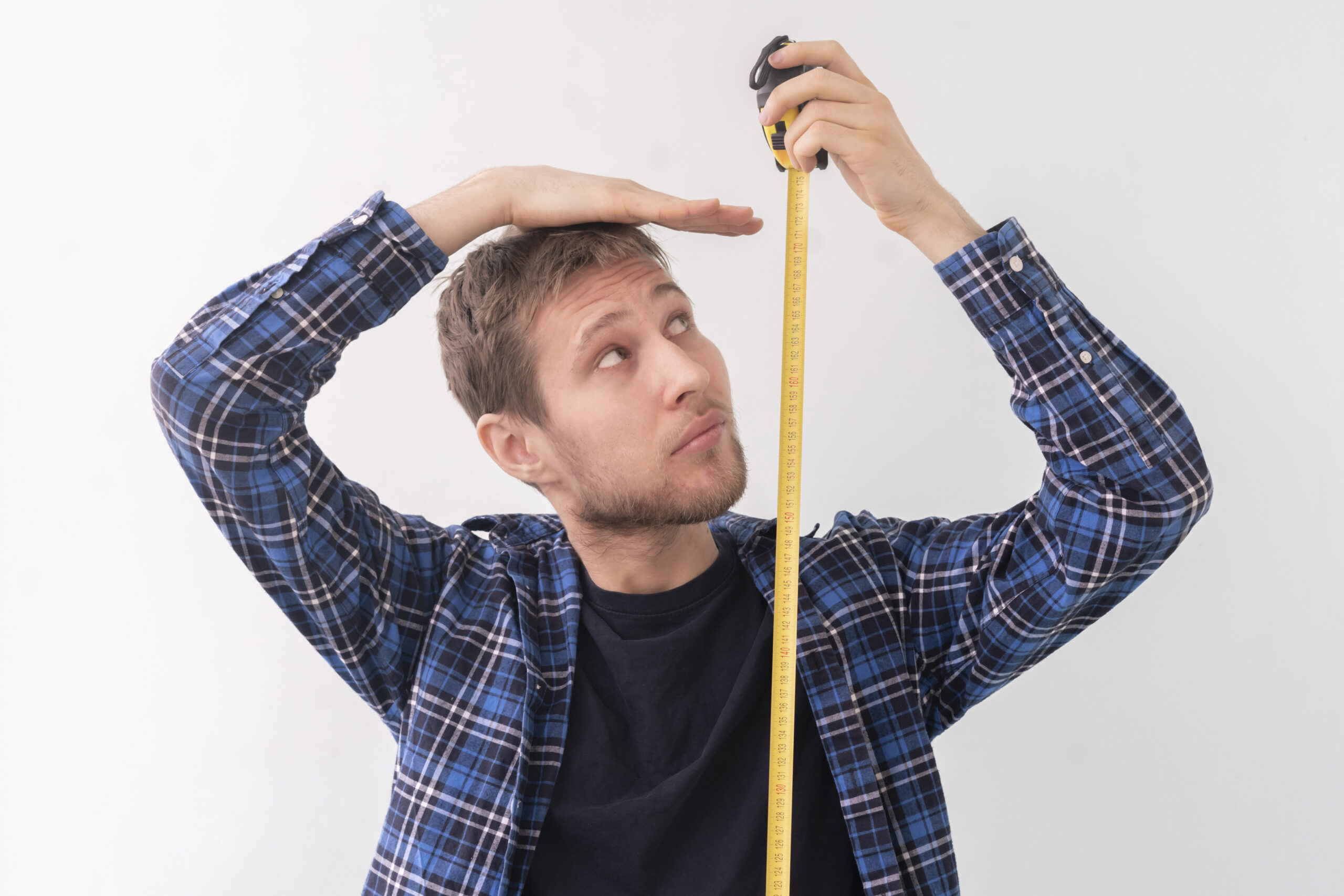 a simple adult teenager male person with a roll tape measure the height against the wall