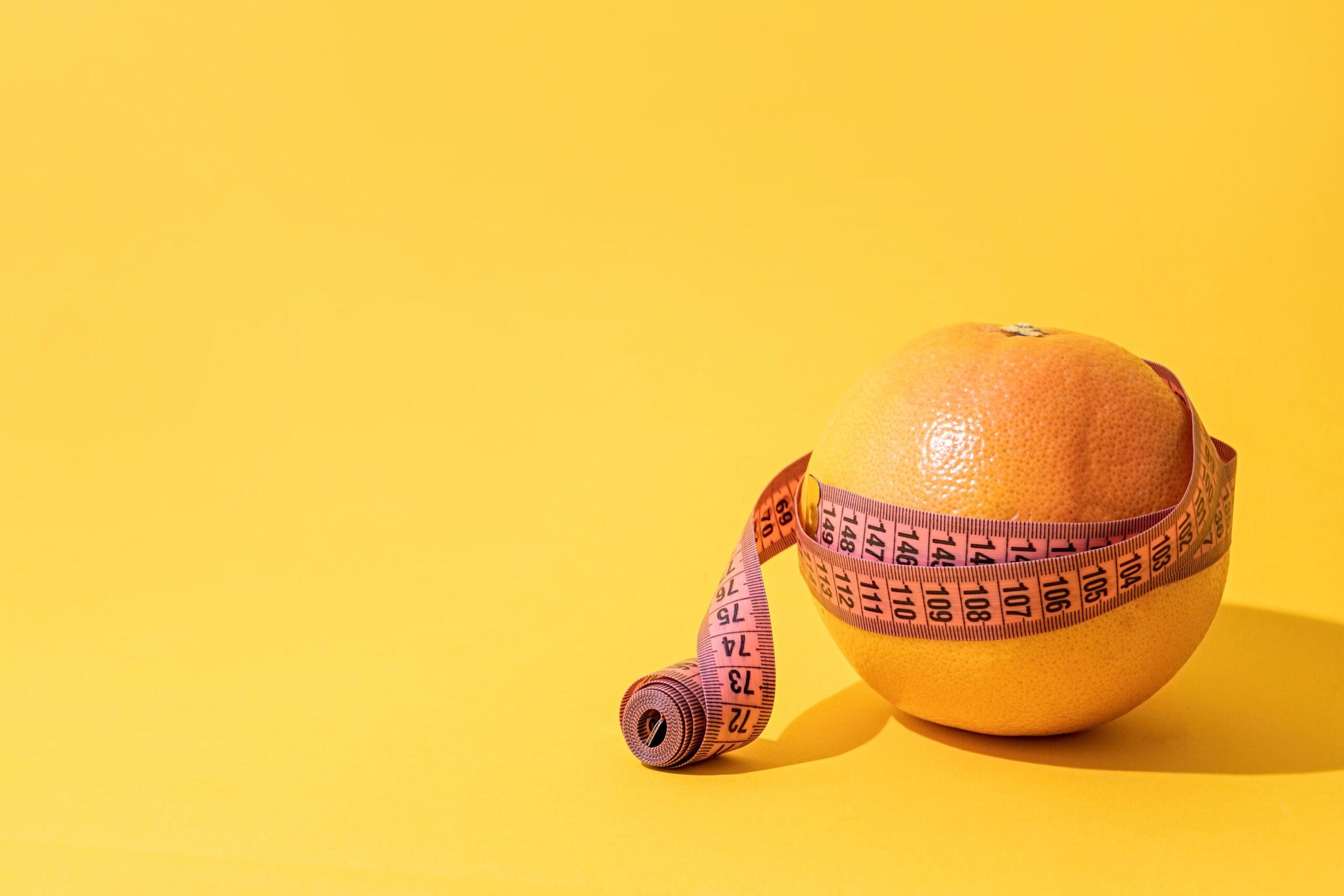 Fruit orange is wrapped with measuring tape on yellow background